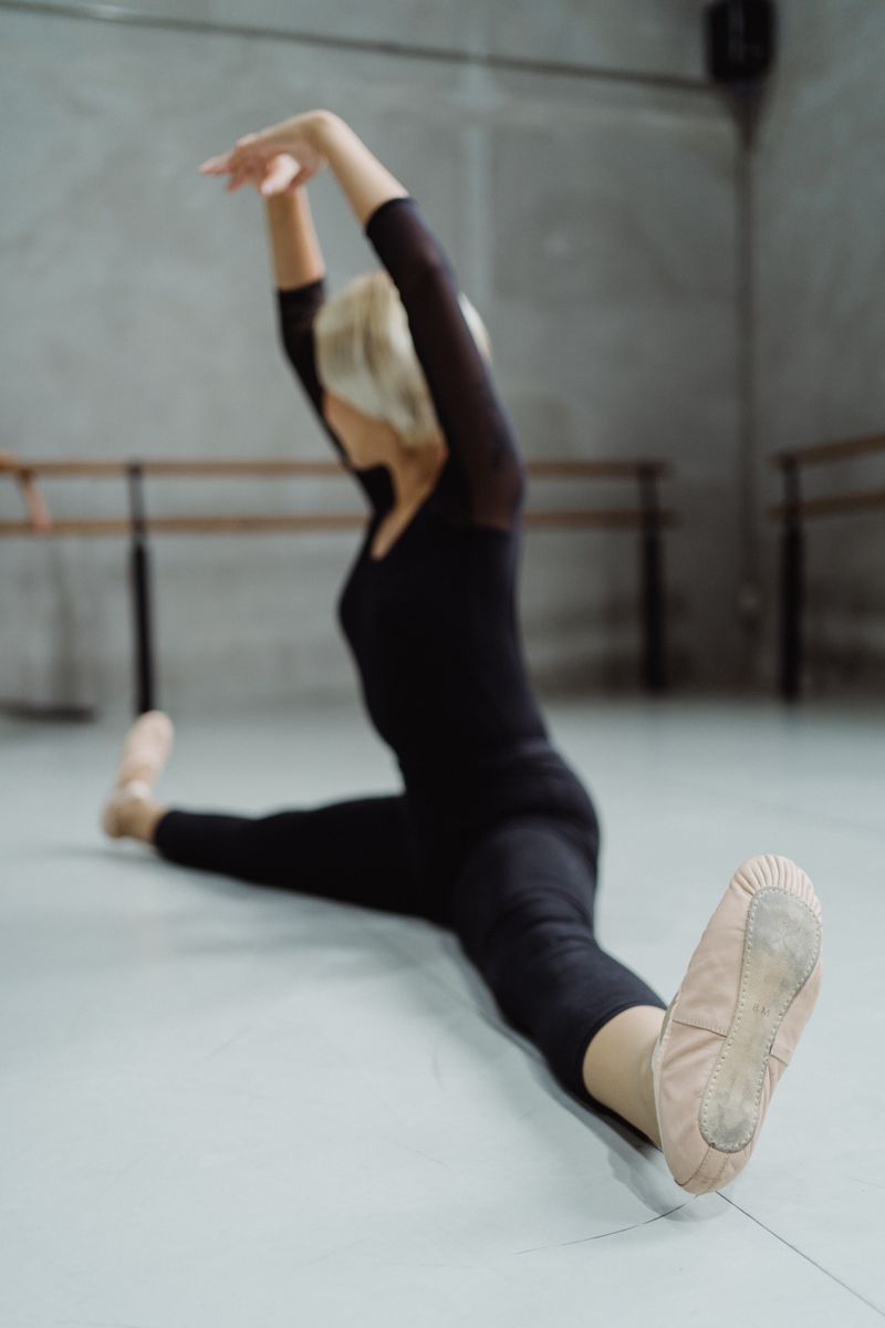 Full body of faceless graceful ballet dancer doing twine posture with hands above head in studio