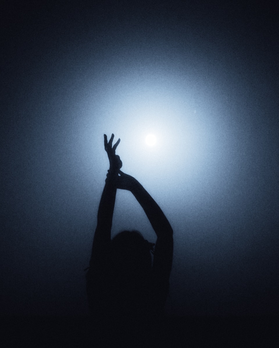 A person in silhouette with arms raised against a bright blue light