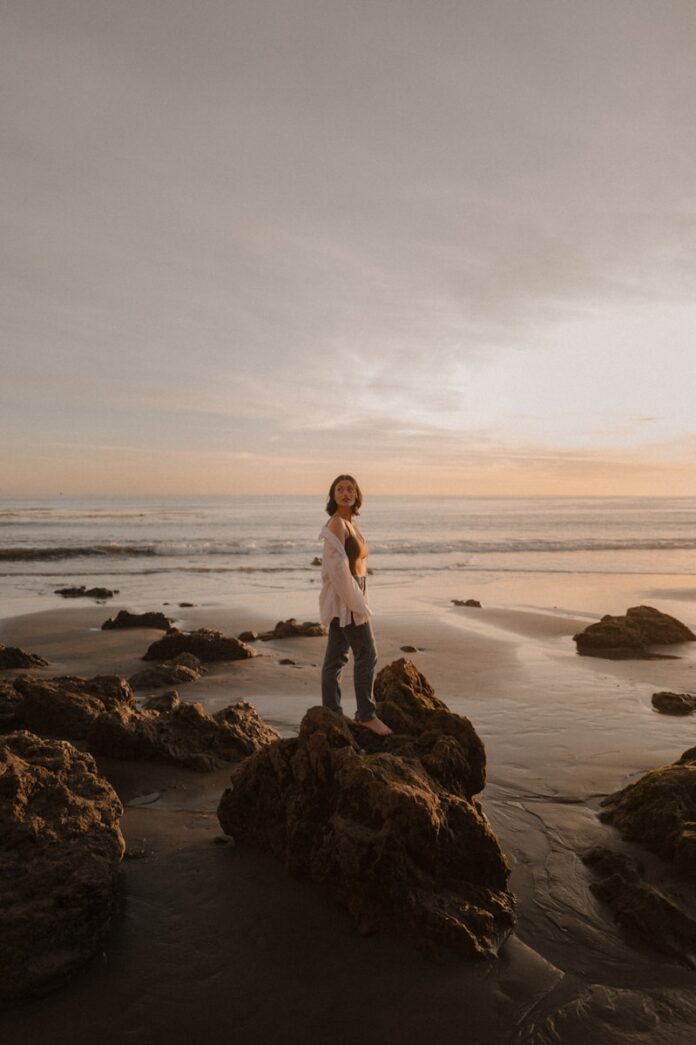 Woman stands on rocks at the beach during sunset.