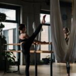 헬스와는 전혀 다른 바레 운동 A woman practices barre exercises in a yoga studio with mirrors and hanging fabric.