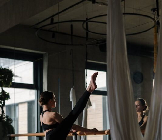 헬스와는 전혀 다른 바레 운동 A woman practices barre exercises in a yoga studio with mirrors and hanging fabric.