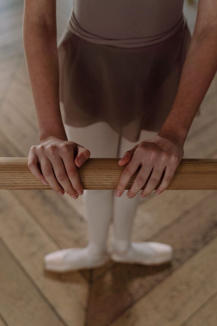 Photo by cottonbro studio A young ballet dancer in uniform practicing at a barre inside a dance studio.