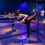 회원이 힘들어했다고 좋은 수업일까요? 오래가는 바레 수업의 비밀 A woman practicing ballet exercises in a studio with mirrors and blue lighting.