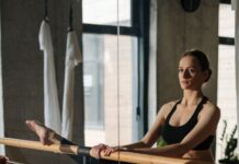 바레 자격증, 고작 3kg인데 운동선수들이 버거워한 이유 A woman in a yoga studio practicing ballet stretches at the barre, emphasizing fitness and wellness.