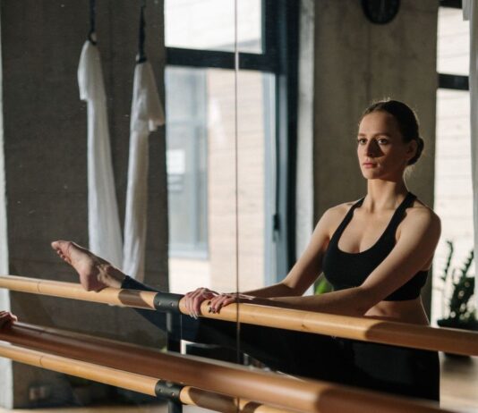바레 자격증, 고작 3kg인데 운동선수들이 버거워한 이유 A woman in a yoga studio practicing ballet stretches at the barre, emphasizing fitness and wellness.