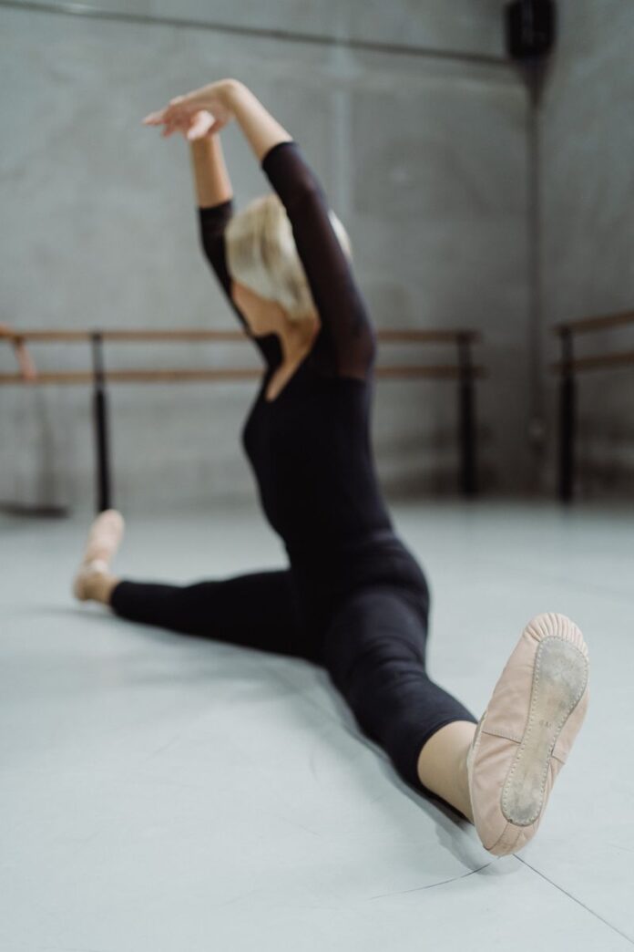 Photo by Budgeron Bach Full body of faceless graceful ballet dancer doing twine posture with hands above head in studio