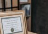 좋은 강사는 자격증 개수로 결정되지 않습니다 Open notebook with magnifying glass on wooden table beside framed certificate.
