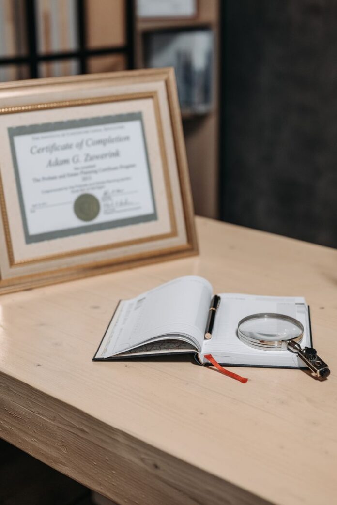 Photo by Pavel Danilyuk Open notebook with magnifying glass on wooden table beside framed certificate.