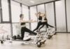 매봉역 필라테스 & 바레 추천, 체형교정이 먼저인 이유 Three women engaged in Pilates exercises on reformer machines in a bright, modern gym setting.