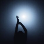 바레 동작 100개 외워도 소용없습니다|회원의 몸을 바꾸는 건 따로 있습니다 A person in silhouette with arms raised against a bright blue light
