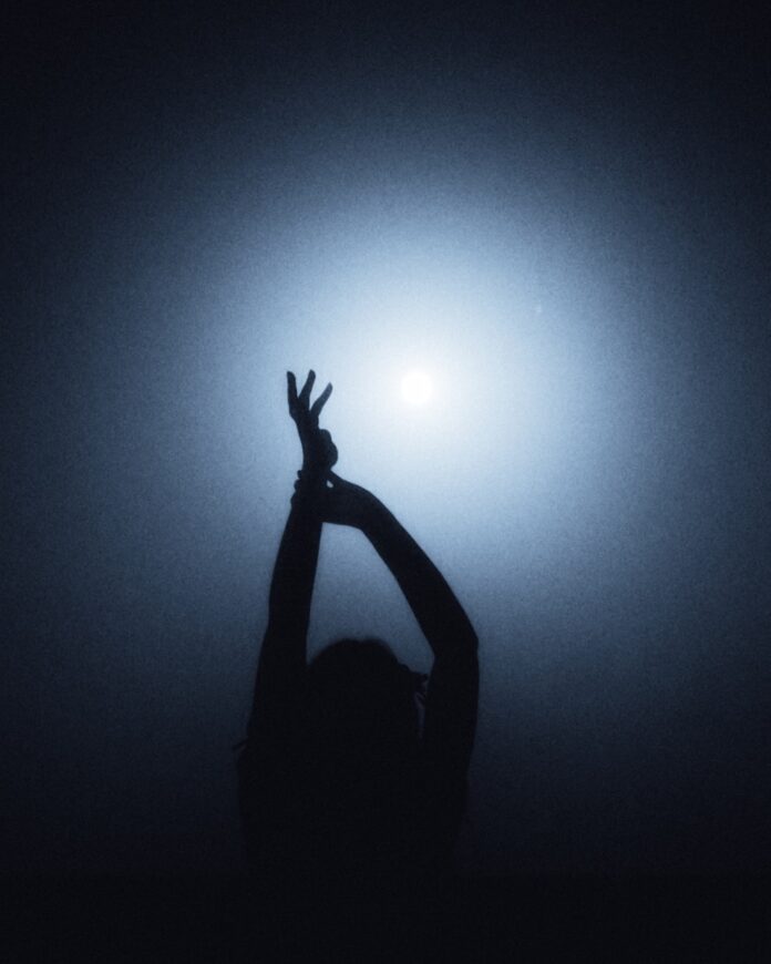 Photo by Max Ovcharenko A person in silhouette with arms raised against a bright blue light